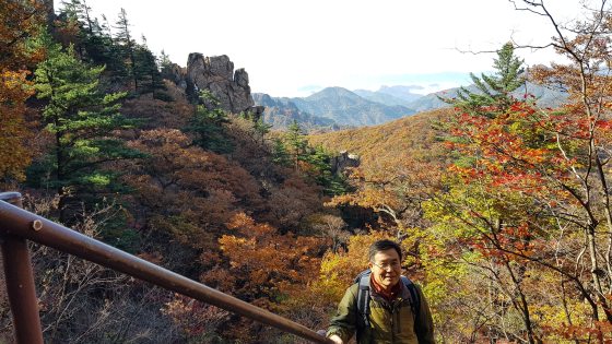 A person looking at the camera, holding the railing of a staircase up in a mountain range.